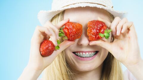 Mädchen häl sich Erdbeeren vor die Augen und lächelt breit dabei