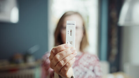 Frau zu Hause mit einem Corona-Selbsttest in der Hand.