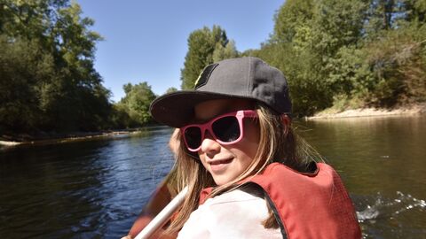 Kind mit Sonnenbrille sitzt lachend im Kanu auf einem Fluss