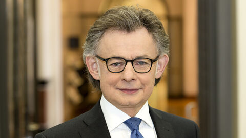 Michael Bußer lächelt frontal in die Kamera. Er ist bis zur Brust zu sehen, trägt ein weißes Hemd, ein schwarzes Sakko und eine blaue Krawatte.