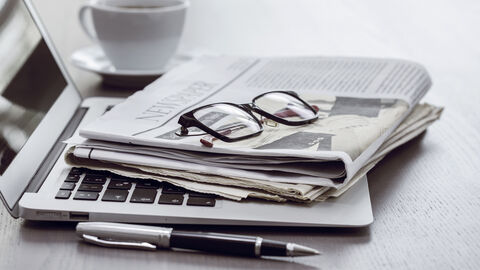 Zeitung und Brille liegen auf Laptop