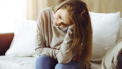 Erschöpfte Frau sitzt auf Couch mit ihrem Kopf auf die Hand gestützt