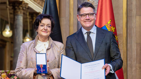 Zwei Personen stehen nebeneinander und halten die Auszeichnung hoch.