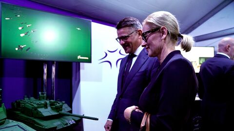 Ministerpräsident Rhein steht mit einer Frau vor einem Miniaturpanzer