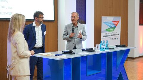 Staatsminister Axel Wintermeyer steht mit zwei weiteren Personen hinter einem Rednerpult der IHK und spricht in ein Mikrofon.