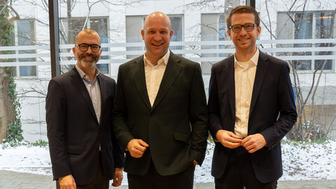 Drei Männer stehen vor einer verglasten Wand