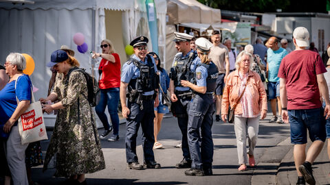 Drei Einsatzkräfte unterhalten sich - um sie herum sieht man Stände und Besucher des Hessentags